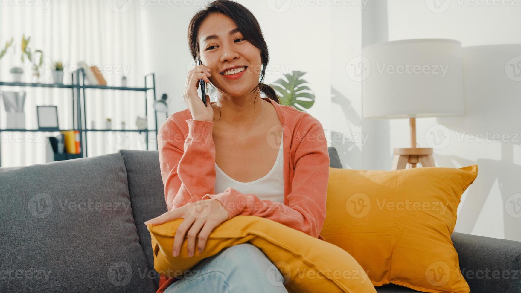 hermosa dama de asia sentada en el sofá llamada telefónica hablar con un amigo en casa. quedarse en casa, relación a larga distancia, relación familiar, mantener la distancia, concepto de cuarentena covid. foto