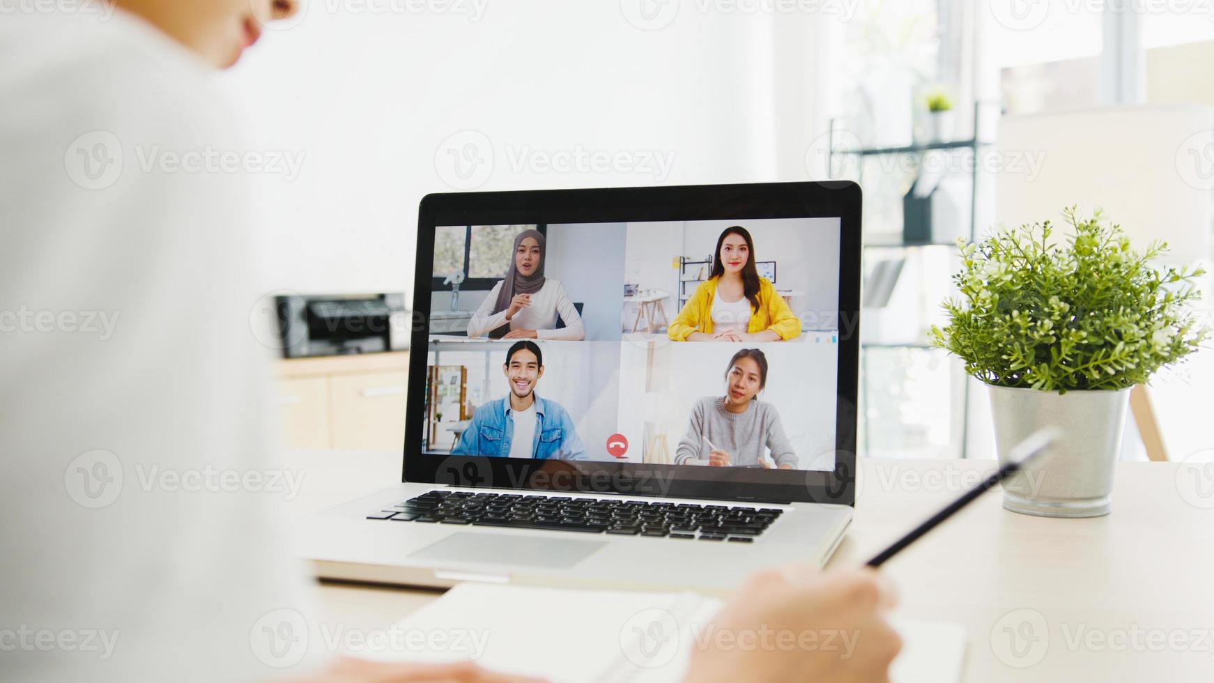 Asia businesswoman using laptop talk to colleagues about plan in video call meeting while working from home at living room. Self-isolation, social distancing, quarantine for corona virus prevention. photo