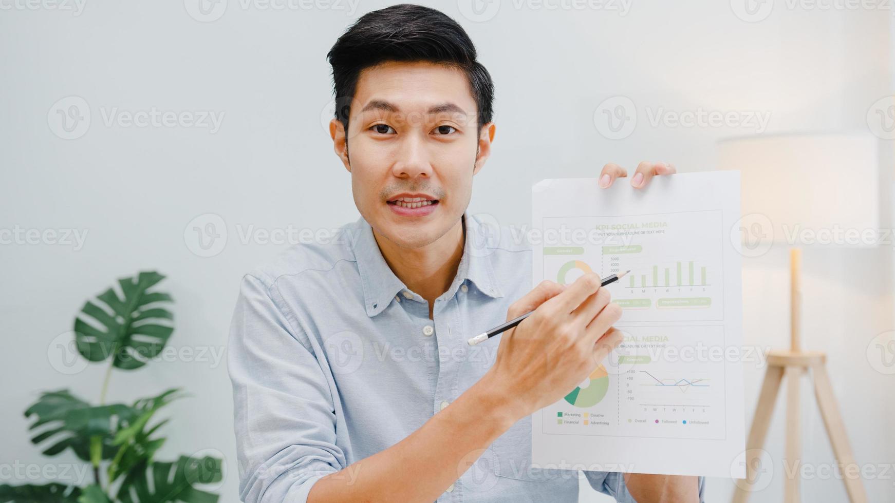 Asia businessman social distancing in new normal situation for virus prevention looking at camera presentation to colleague about plan in video call while work in office. Lifestyle after corona virus. photo