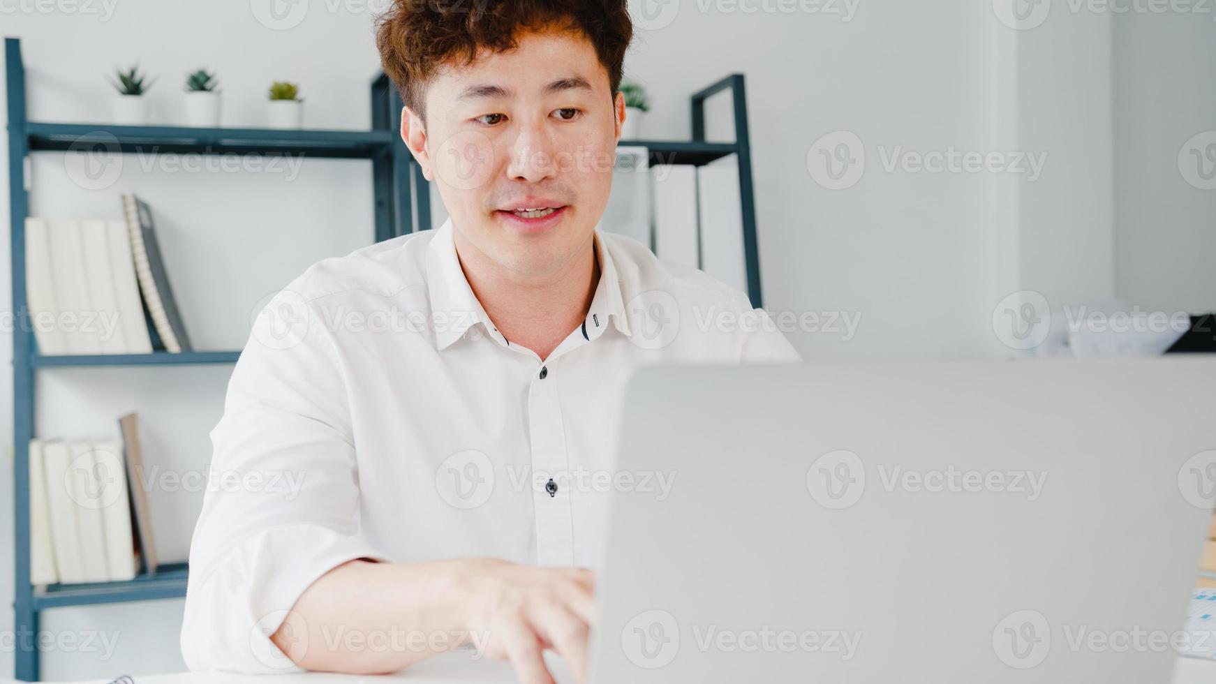 Young Asia businessman using laptop talk to colleagues about plan in video call while smart working from home at living room. Self-isolation, social distancing, quarantine for corona virus prevention. photo