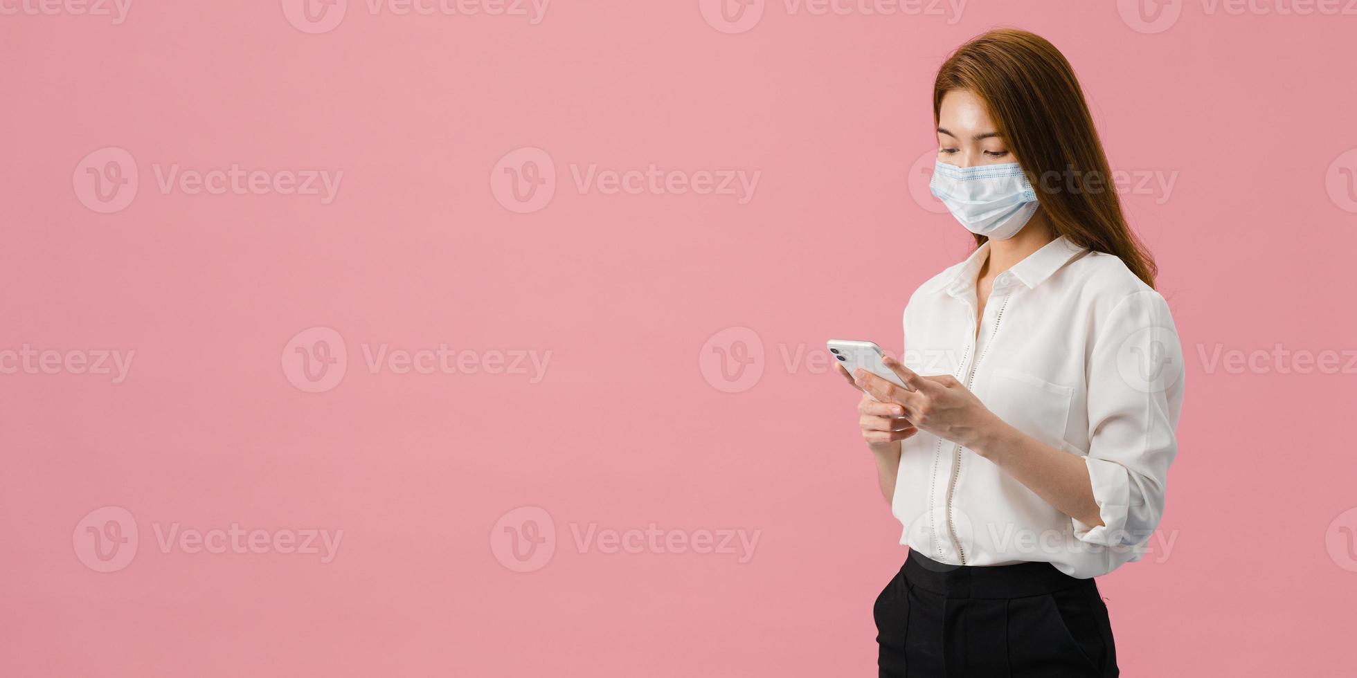 La muchacha joven de Asia usa el teléfono móvil del uso de la mascarilla médica con vestida con ropa casual. autoaislamiento, distanciamiento social, cuarentena por coronavirus. Pancarta panorámica de fondo rosa con espacio de copia. foto