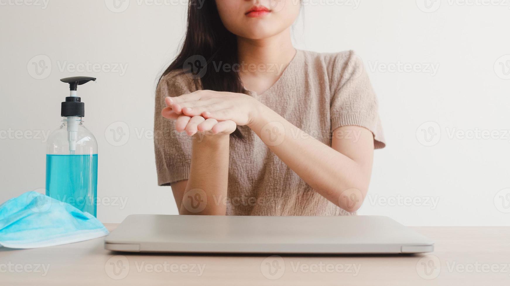 Asian woman using alcohol gel hand sanitizer wash hand before open laptop for protect coronavirus. Female push alcohol to clean for hygiene when social distancing stay at home and self quarantine time photo