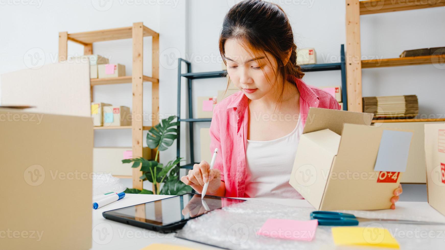 joven empresaria empresaria de asia comprobar la orden de compra del producto en stock y guardar en la computadora de tableta el trabajo en la oficina en casa. propietario de una pequeña empresa, entrega de mercado en línea, concepto independiente de estilo de vida. foto