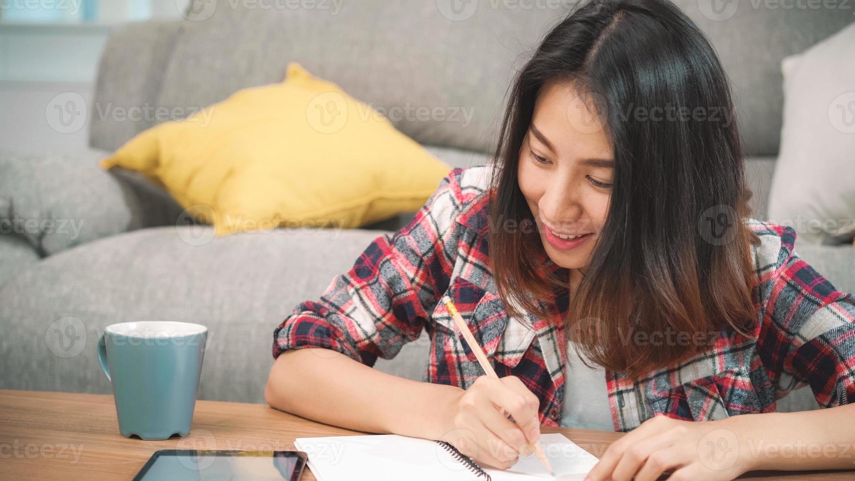 mujer estudiante asiática hacer la tarea en casa, mujer usando tableta para buscar en el sofá en la sala de estar en casa. las mujeres de estilo de vida se relajan en el concepto de hogar. foto