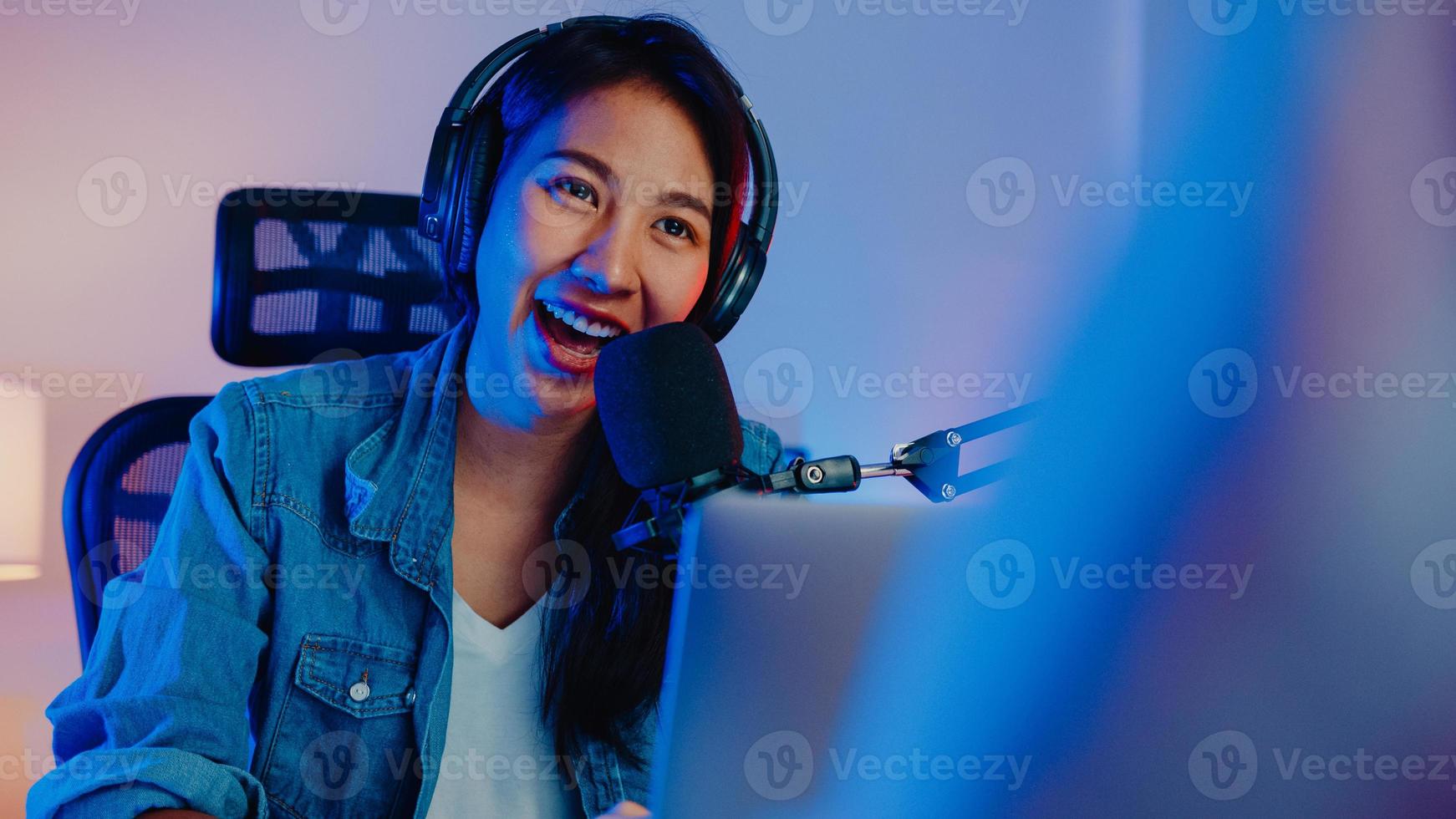 Happy asia girl host record podcast use microphone wear headphone with laptop interview guest conversation for content in her home studio at night. Sound equipment concept. Content creator concept. photo