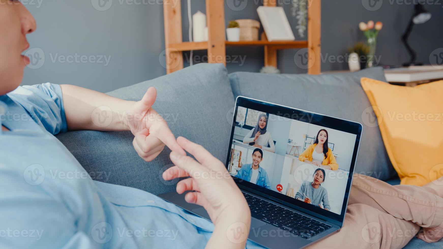 Young Asia businessman using laptop talk to colleagues about plan in video call meeting while work from home at living room. Self-isolation, social distancing, quarantine for corona virus prevention. photo