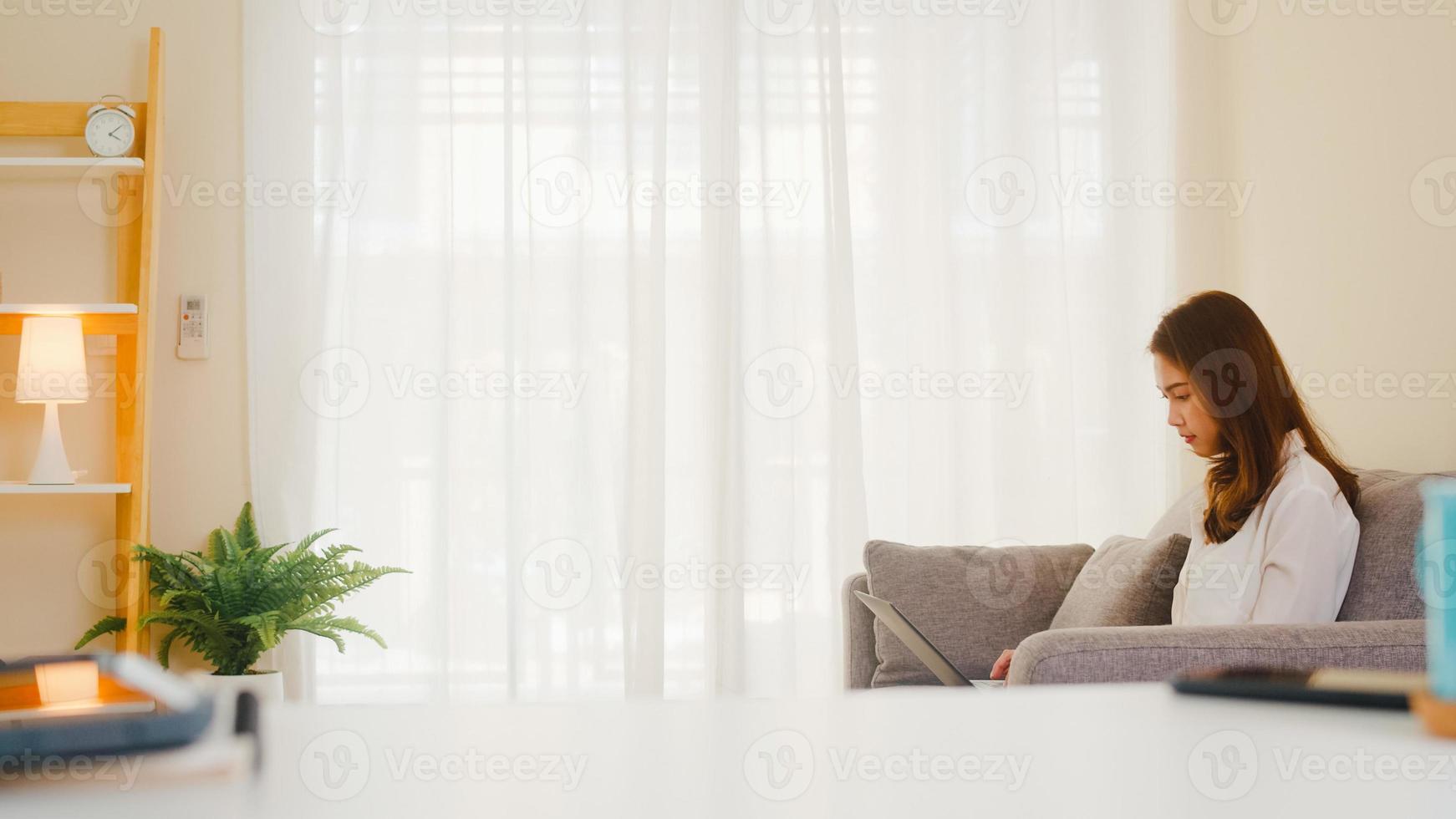 Retrato de ropa casual de mujeres asiáticas independientes usando una computadora portátil que trabaja en la sala de estar en casa. trabajo desde casa, trabajo a distancia, autoaislamiento, distanciamiento social, cuarentena para la prevención del coronavirus. foto