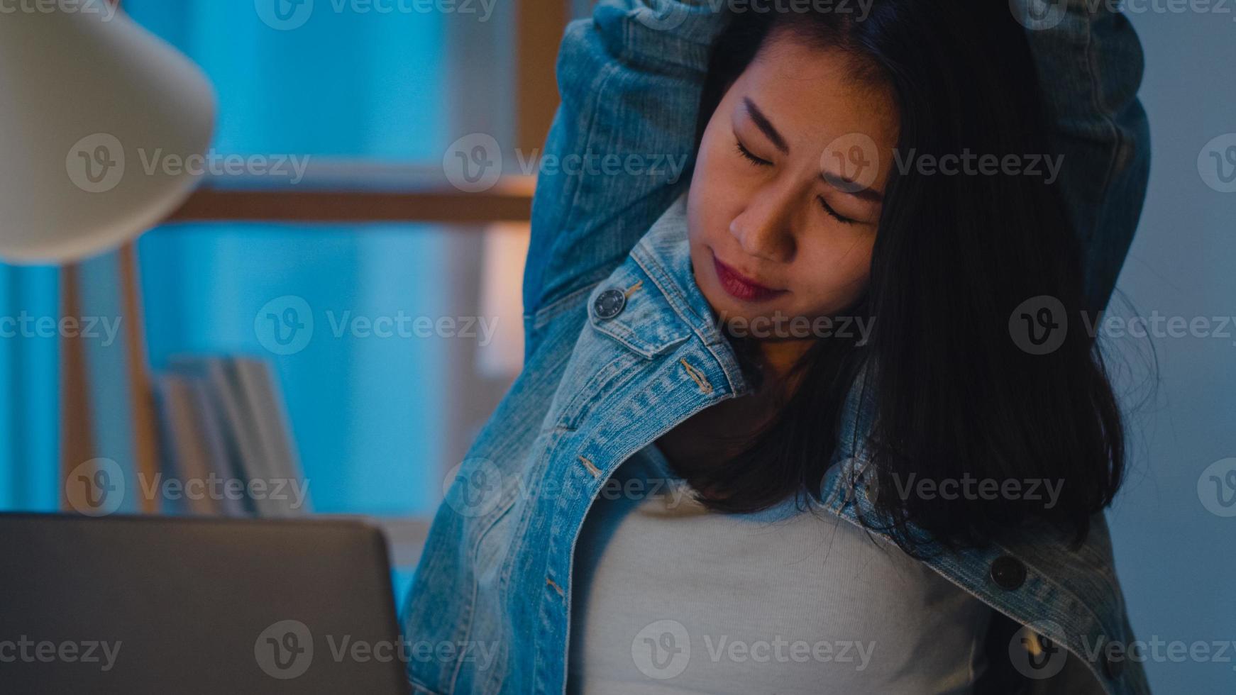 Millennial young Chinese businesswoman working late night stretching on her chair, looking in laptop computer in living room at modern home. Asia people occupational burnout syndrome concept. photo