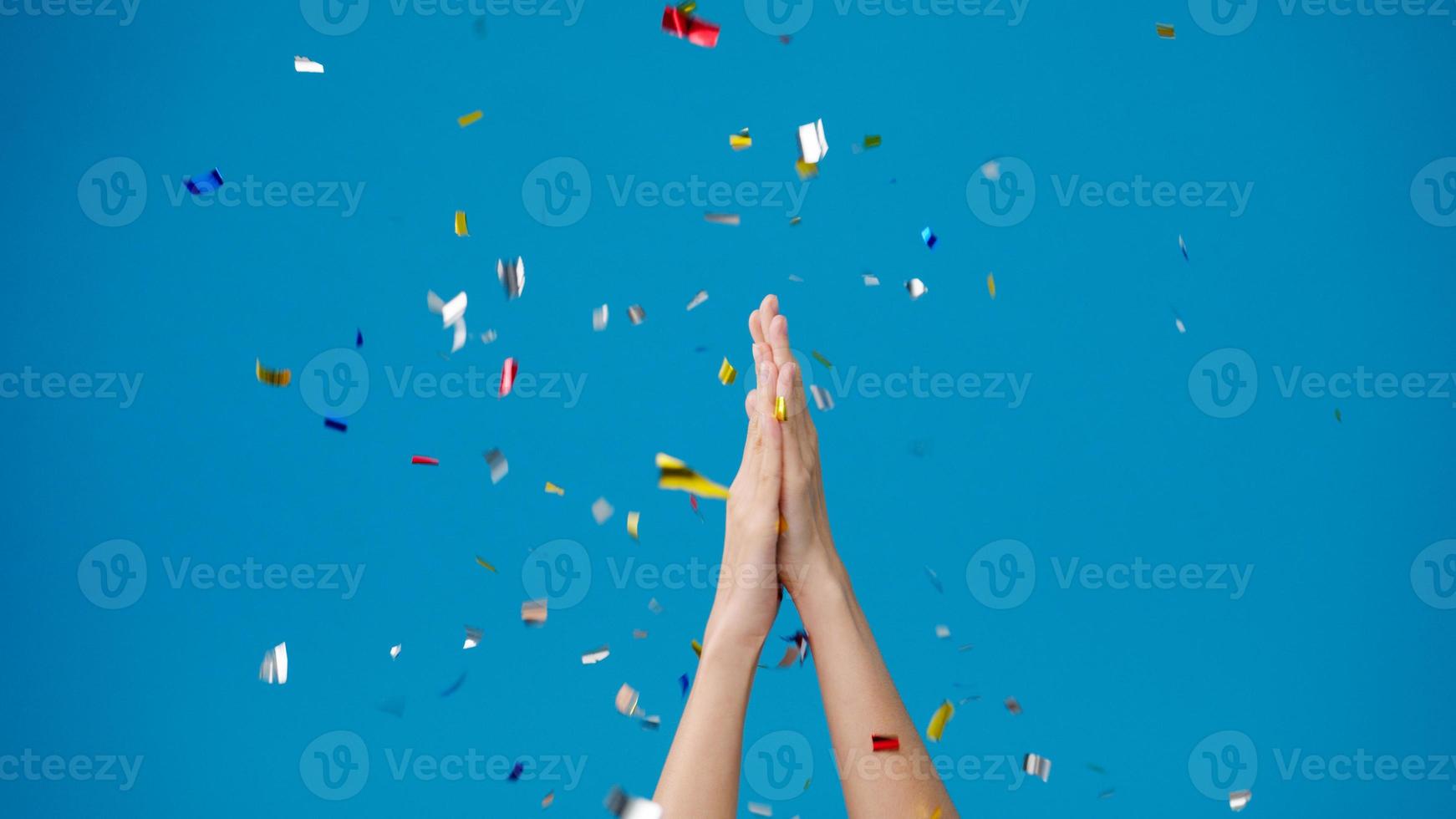 niña muestra la mano aplaudiendo aplausos bajo la lluvia de confeti y celebrando sobre fondo azul. Copie el espacio para colocar un mensaje de texto, para publicidad. área publicitaria, simulacro de contenido promocional. foto