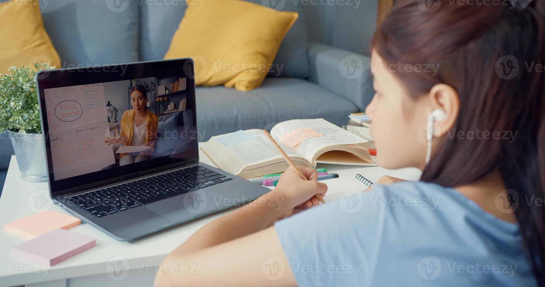 Young Asia girl with casual use computer laptop video call learn online with teacher write lecture notebook living room at house. Isolate education online e-learning coronavirus pandemic concept. photo
