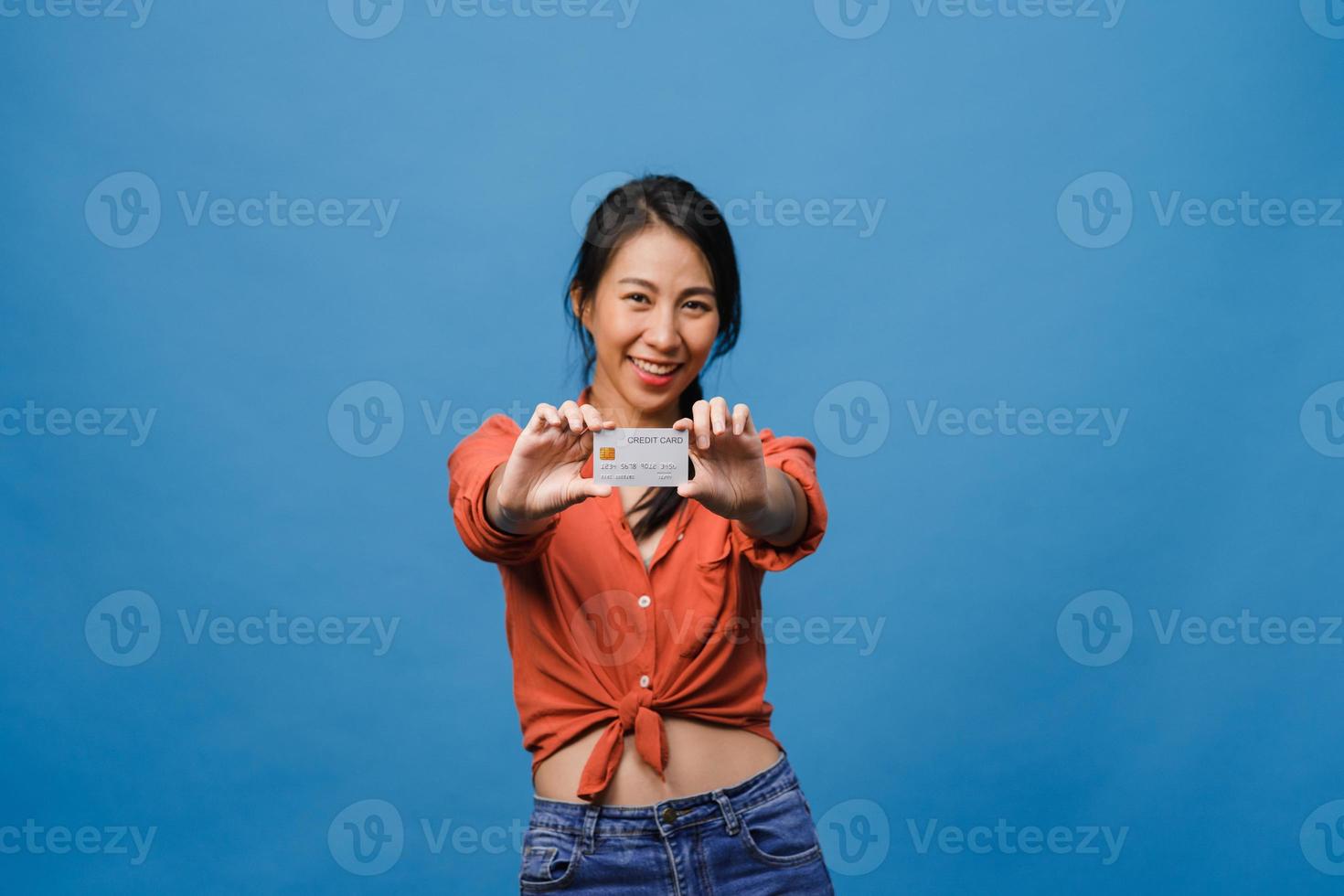 Young Asia lady show credit bank card with positive expression, smiles broadly, dressed in casual clothing feeling happiness and stand isolated on blue background. Facial expression concept. photo