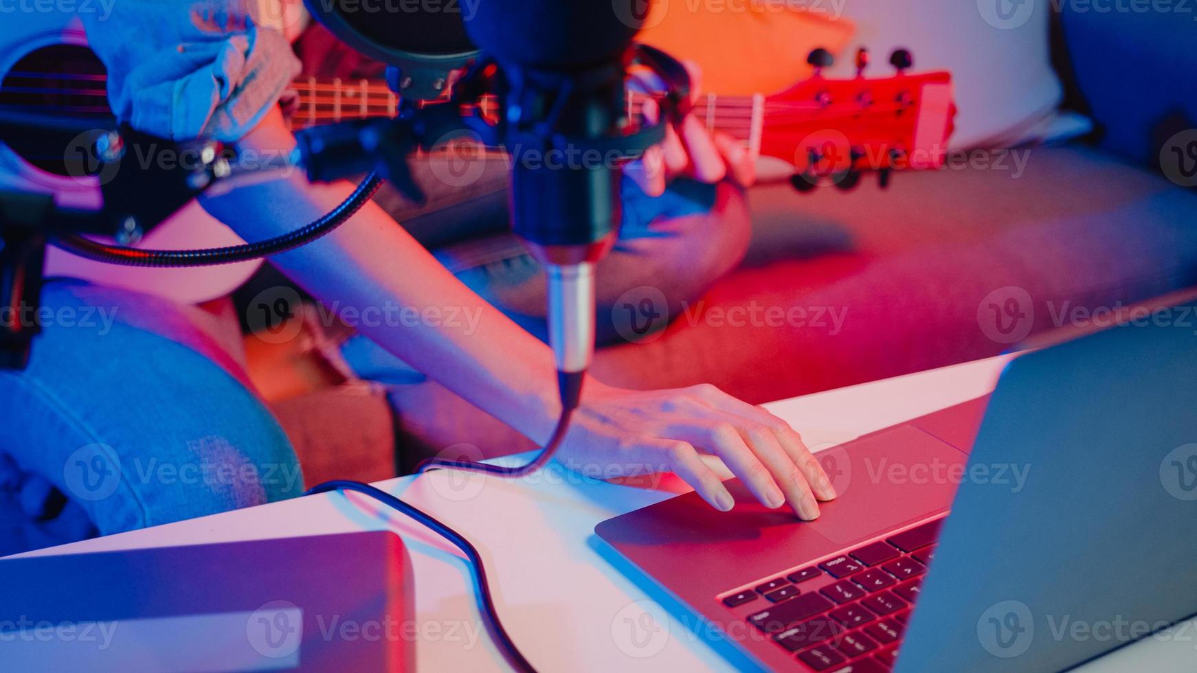 Happy asia girl blogger play guitar and use microphone sing song record music sound mixer on laptop in modern living room home studio at night. Music content creator, Tutorial, Broadcast concept. photo