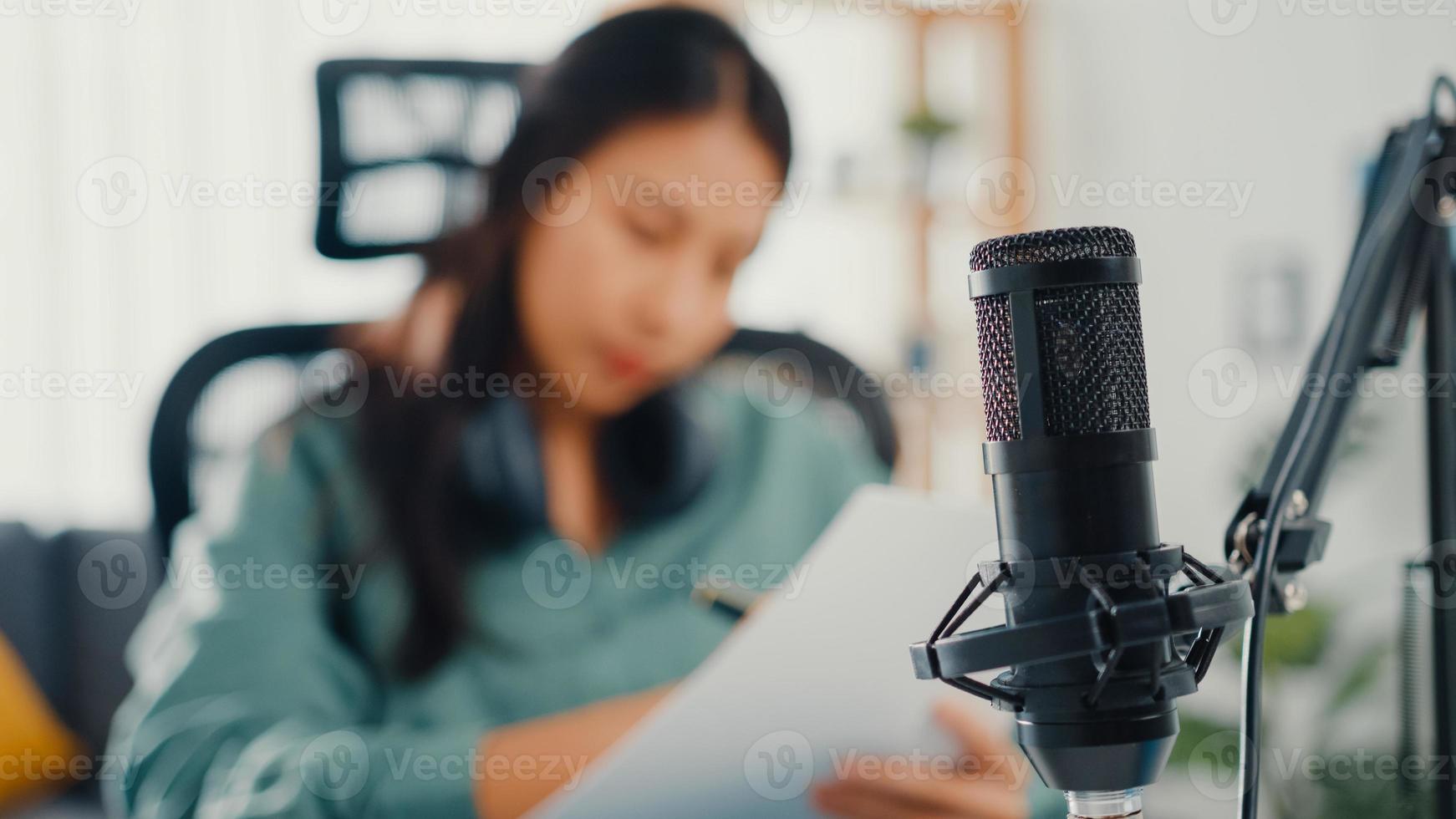 Attractive asia girl record podcast use microphone hold paper creating content for audio blog talk and practice for review topic in her room. Make audio podcast from home,  Sound equipment concept. photo