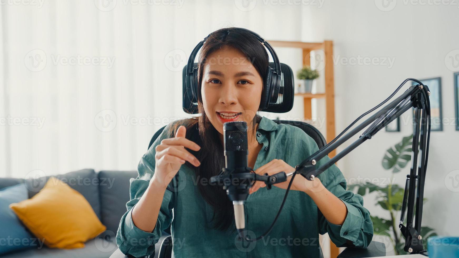 feliz niña asiática grabar un podcast con auriculares y micrófono, mirar a la cámara, hablar y descansar en su habitación. Podcaster femenina hace podcast de audio desde su estudio en casa, permanece en el concepto de casa. foto