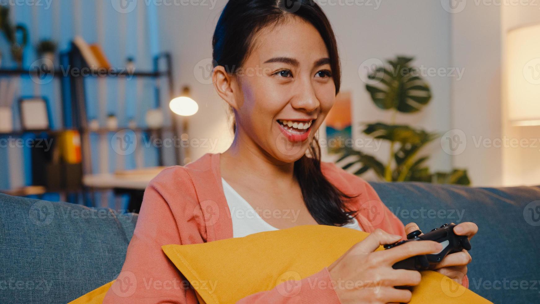 Young Asia lady using wireless controller play video game having funny happy moment on sofa in living room at home night. Stay at house, Self quarantine activity for covid or coronavirus quarantine. photo