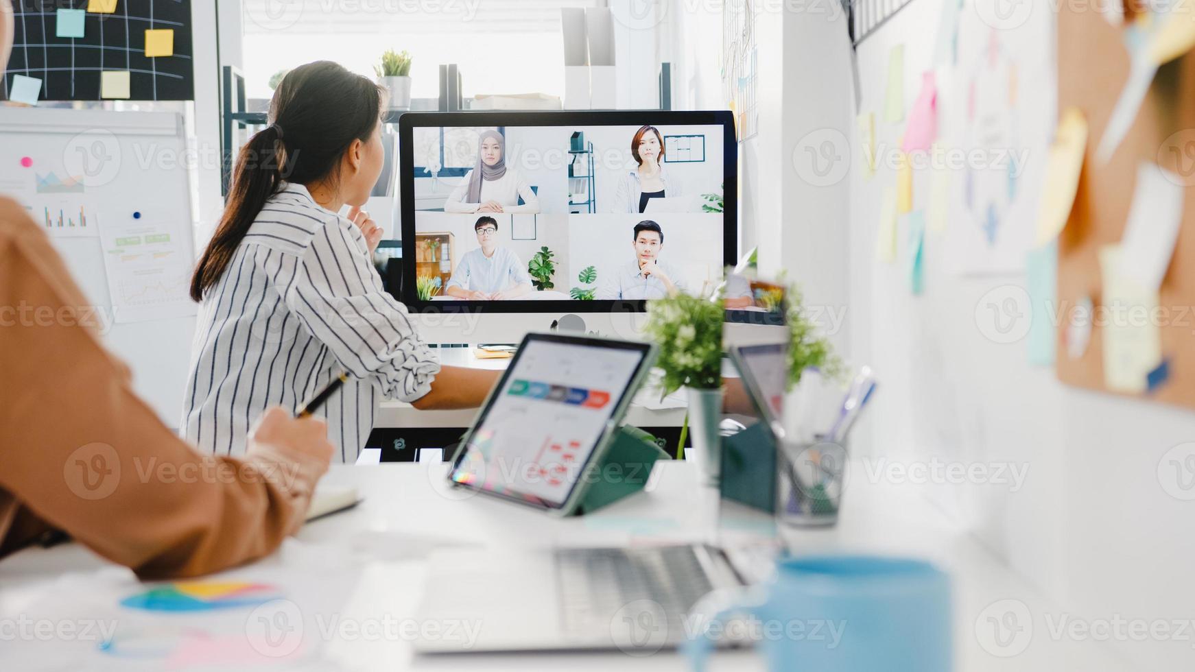 Asia businesspeople using desktop talk to colleagues discussing business brainstorm about plan in video call meeting in new normal office. Lifestyle social distancing and work after corona virus. photo