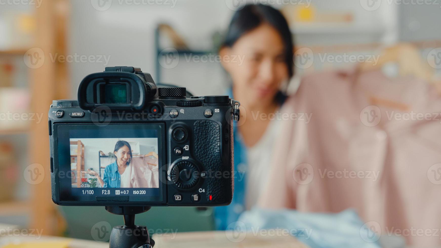 joven diseñadora de moda asiática que usa un teléfono móvil y recibe una orden de compra y muestra la ropa, grabando video en vivo en línea con la cámara. propietario de una pequeña empresa, concepto de entrega de mercado en línea. foto