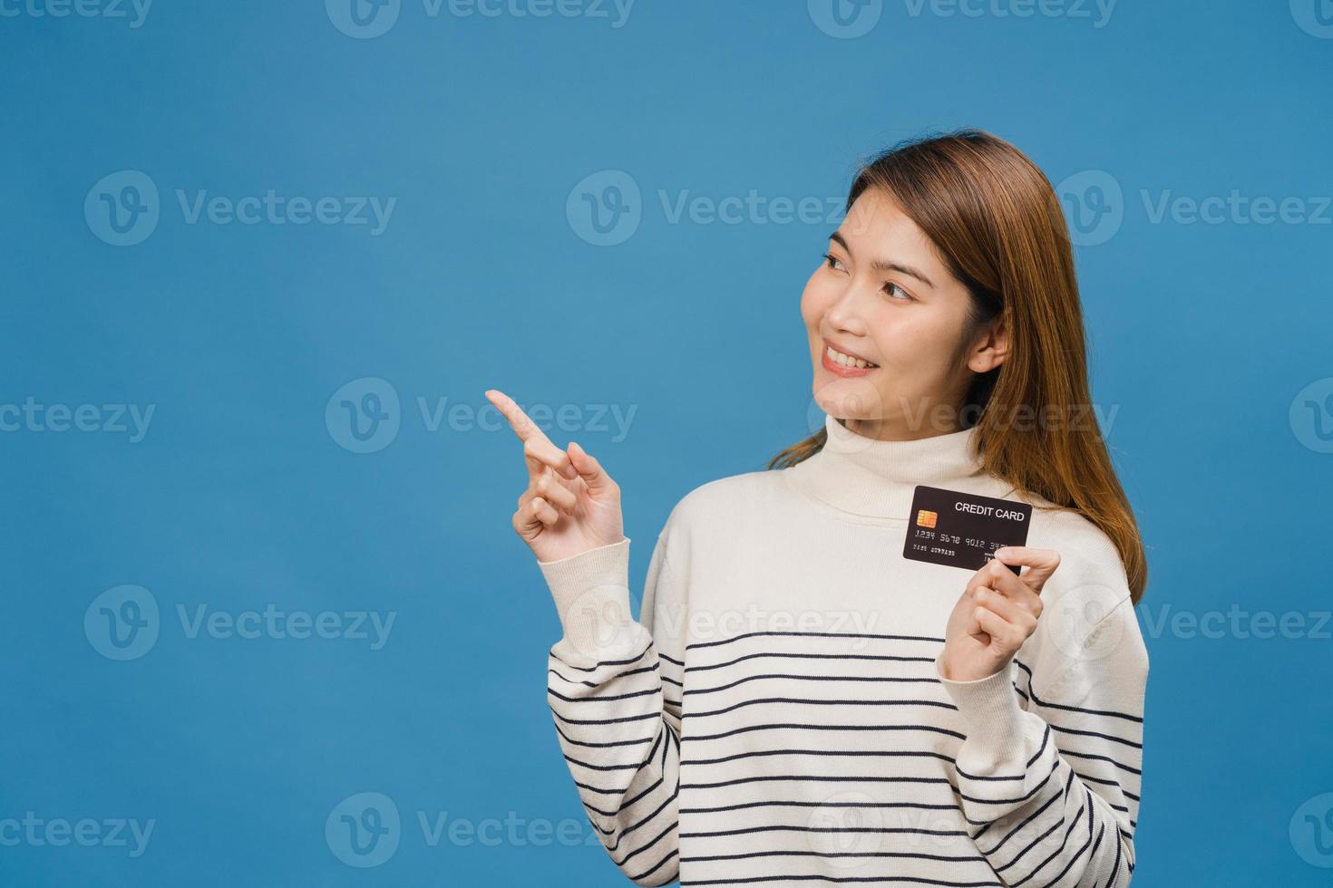 Young Asia lady show credit bank card with positive expression, smiles broadly, dressed in casual clothing feeling happiness and stand isolated on blue background. Facial expression concept. photo