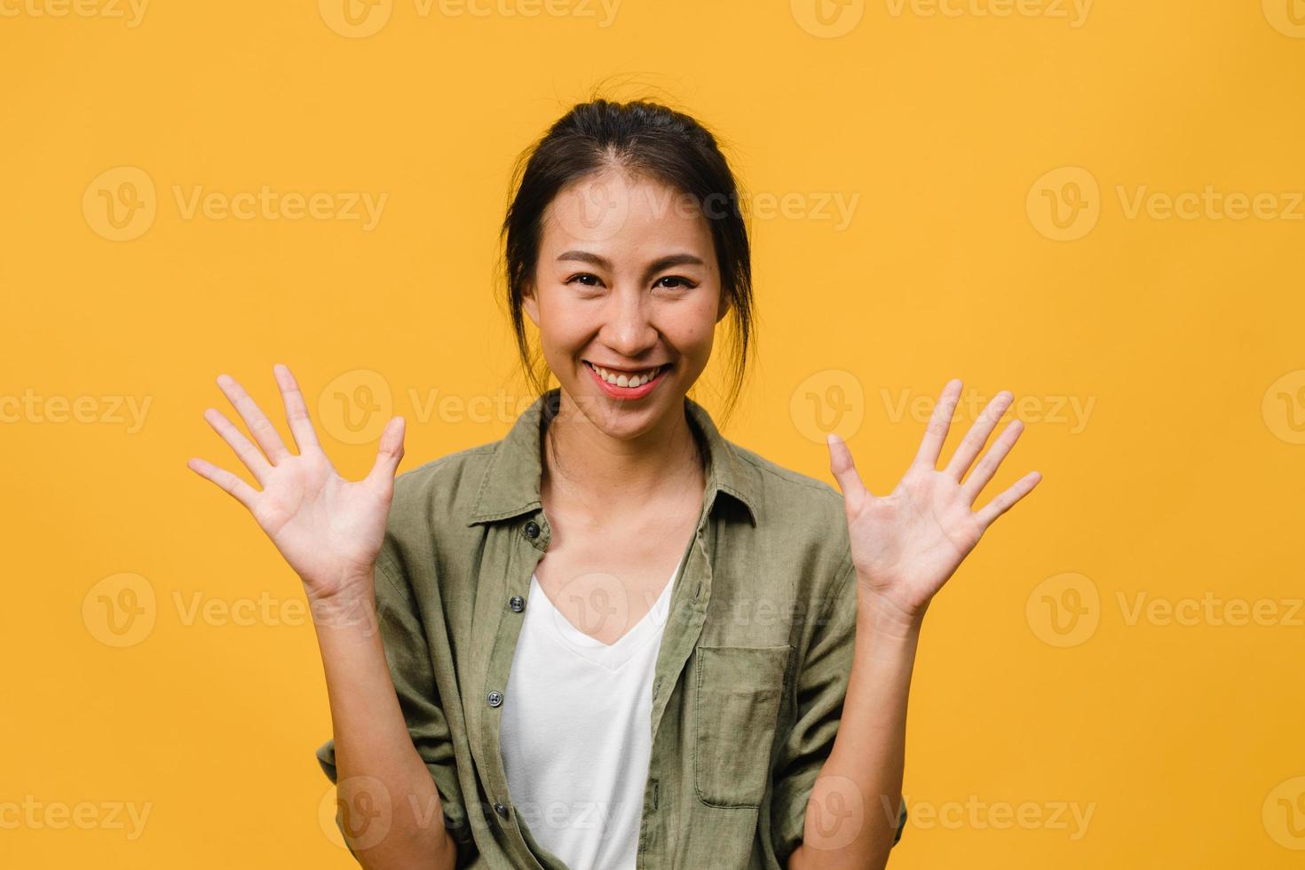 Jovencita asiática con expresión positiva, sonrisa amplia, vestida con ropa casual y mirando a cámara sobre fondo amarillo. feliz adorable mujer alegre se regocija con el éxito. concepto de expresión facial. foto