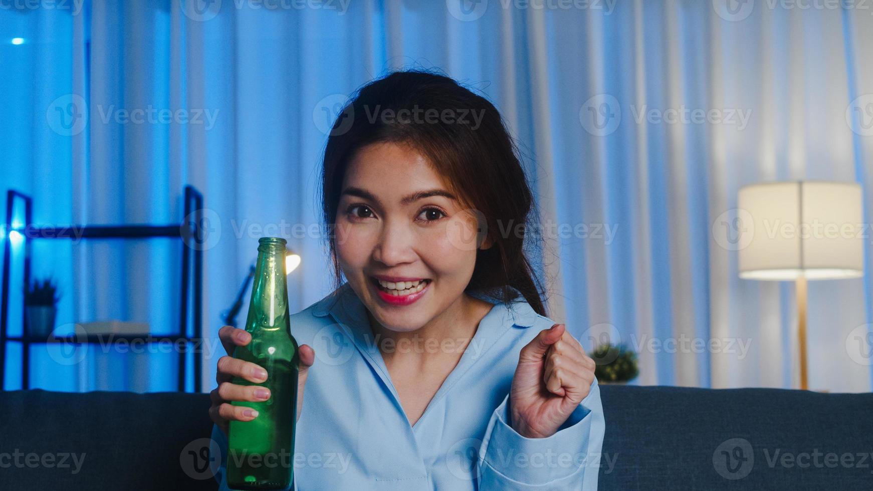 joven asiática bebiendo cerveza divirtiéndose feliz momento fiesta nocturna evento celebración en línea a través de videollamada en la sala de estar en casa. distanciamiento social, cuarentena por coronavirus. punto de vista o pov. foto