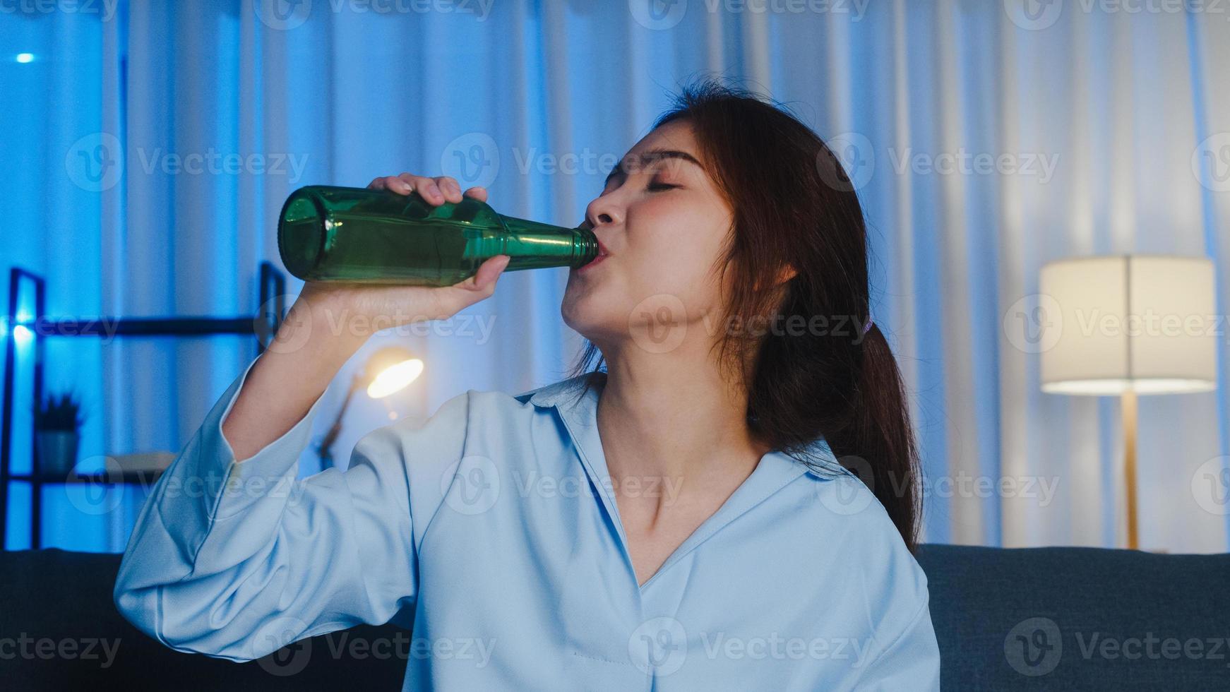 Young Asian lady drinking beer having fun happy moment night party event online celebration via video call in living room at home. Social distancing, quarantine for coronavirus. Point of view or POV. photo