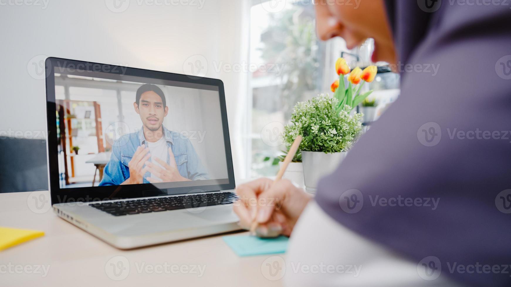 Asia muslim businesswoman using laptop talk to colleague about plan by video call brainstorm online meeting while remotely work from home at living room. Social distancing, quarantine for corona virus photo