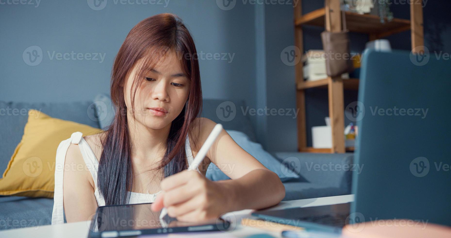 Young Asia girl teenager with casual use computer laptop focus to learn online write lecture in digital laptop in living room at home. Isolate education online e-learning coronavirus pandemic concept. photo