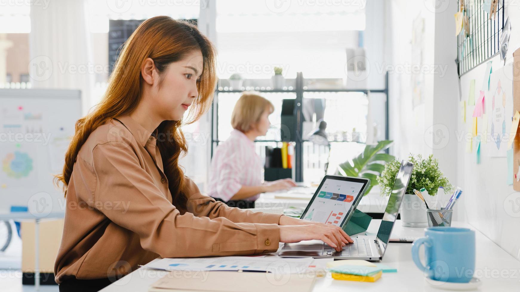 distanciamiento social de la joven empresaria empresaria de asia en una nueva situación normal para la prevención de virus mientras usa una computadora portátil y una tableta en el trabajo en la oficina. estilo de vida después del coronavirus. foto