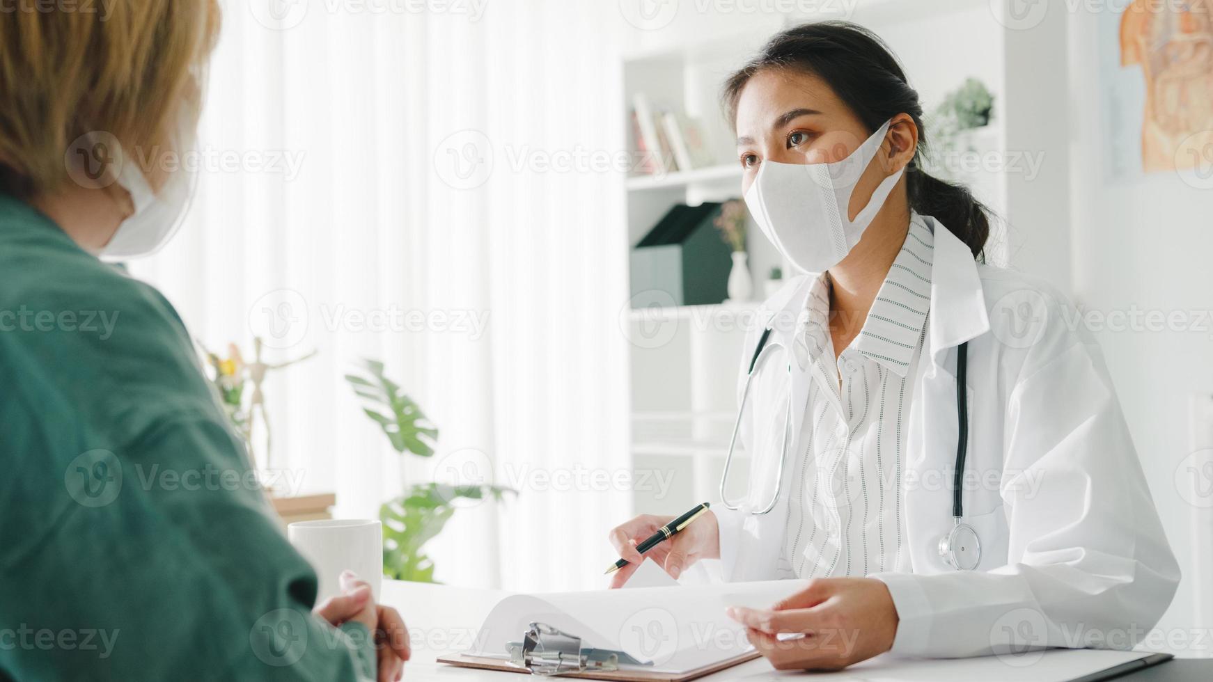 La joven doctora de Asia usa una máscara protectora usando el portapapeles está brindando una gran charla de noticias sobre los resultados o los síntomas con la paciente en la oficina del hospital. estilo de vida nuevo normal después del virus corona. foto