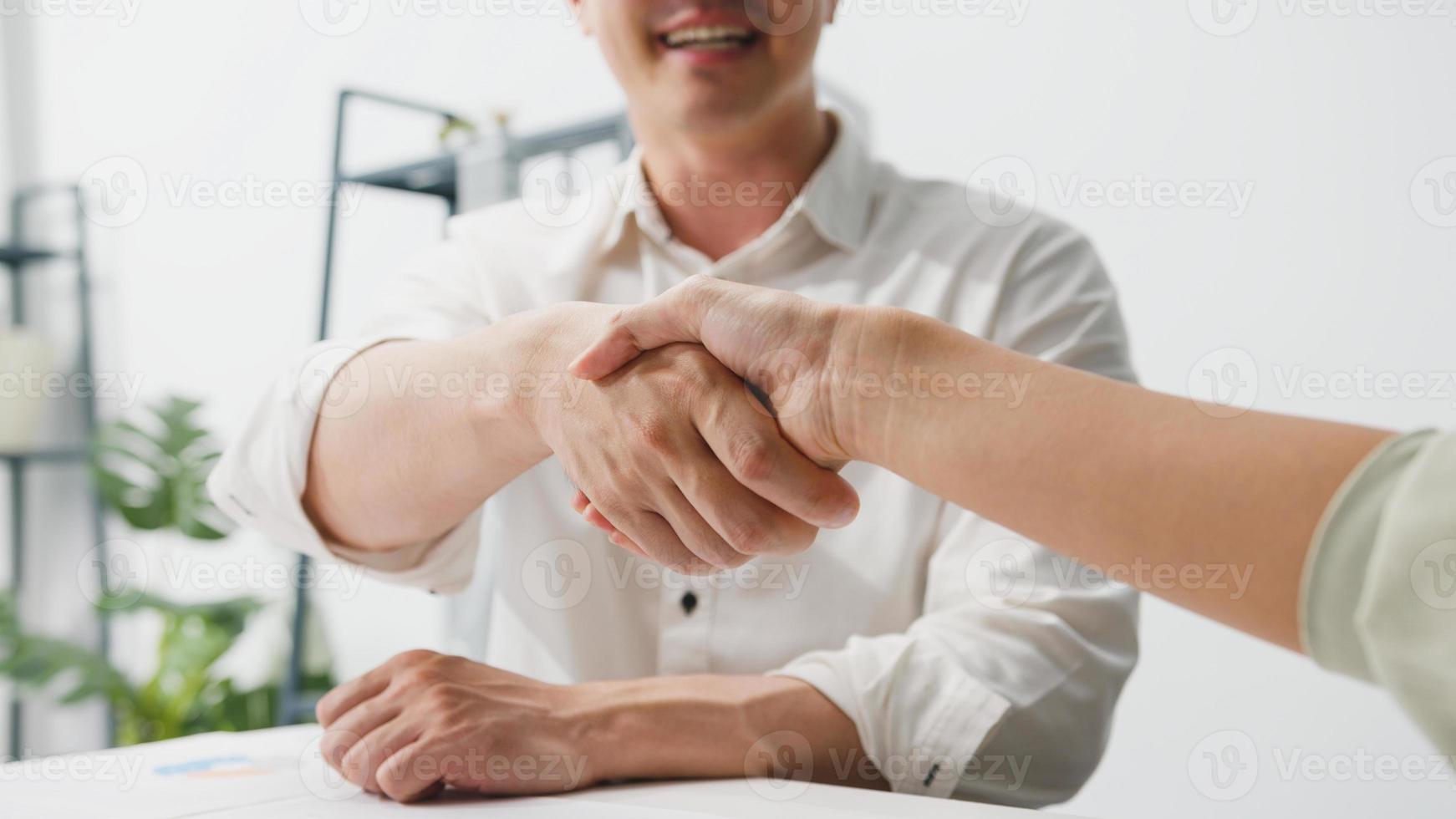 Grupo multirracial de jóvenes creativos en ropa casual elegante discutiendo negocios dándose la mano y sonriendo mientras está sentado en la oficina moderna. cooperación de socios, concepto de trabajo en equipo de compañeros de trabajo. foto