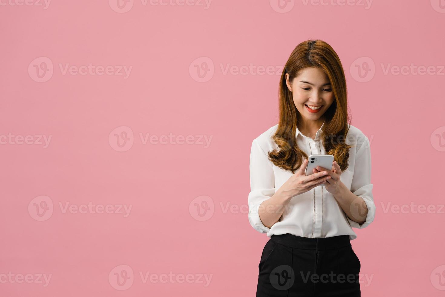 Young Asia lady using phone with positive expression, smiles broadly, dressed in casual clothing feeling happiness and standing isolated on pink background. Happy adorable glad woman rejoices success. photo