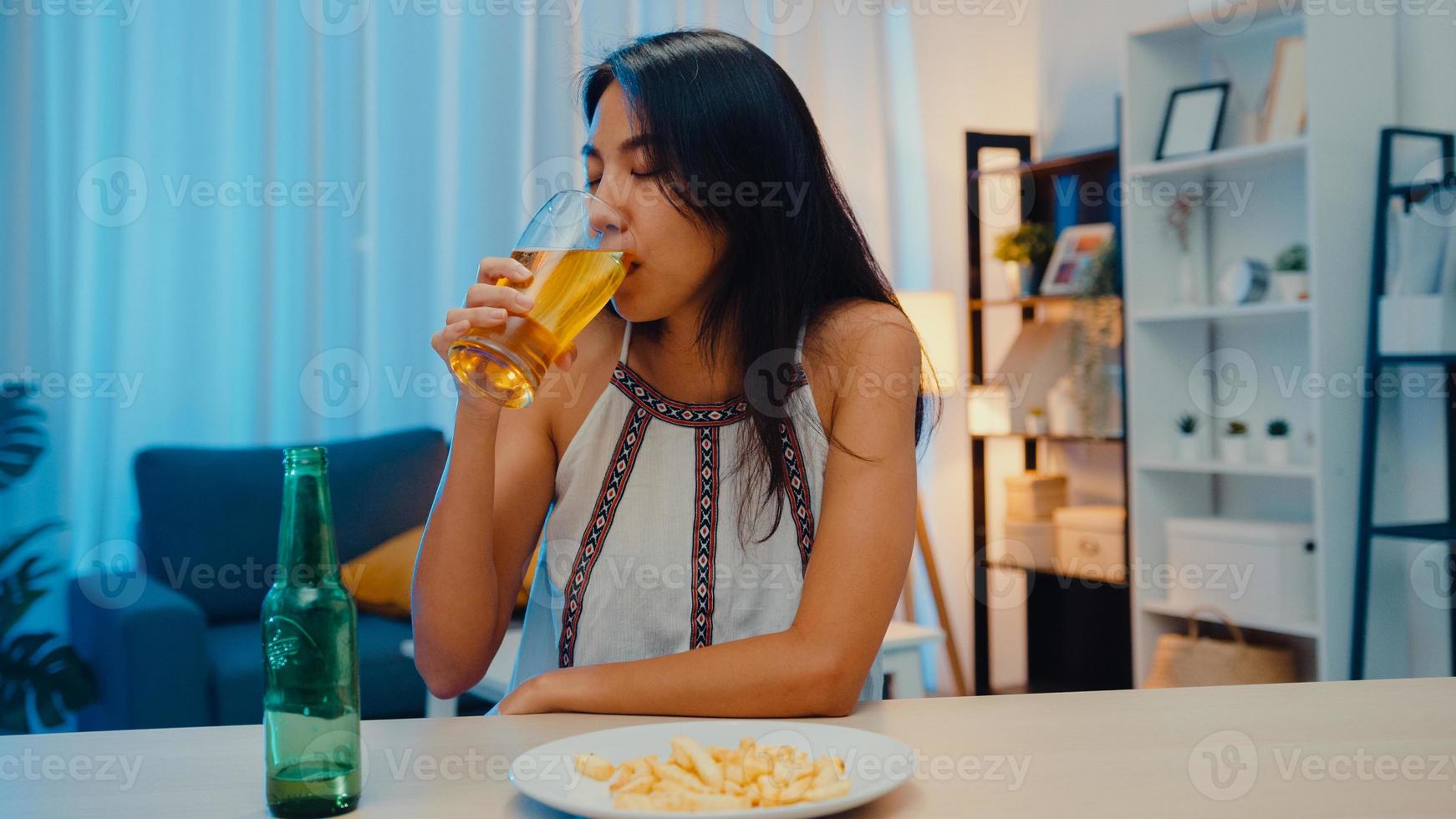 joven asiática bebiendo cerveza divirtiéndose feliz noche fiesta evento de año nuevo celebración en línea a través de videollamada por teléfono en casa por la noche. distancia social, cuarentena por coronavirus. punto de vista o pov foto