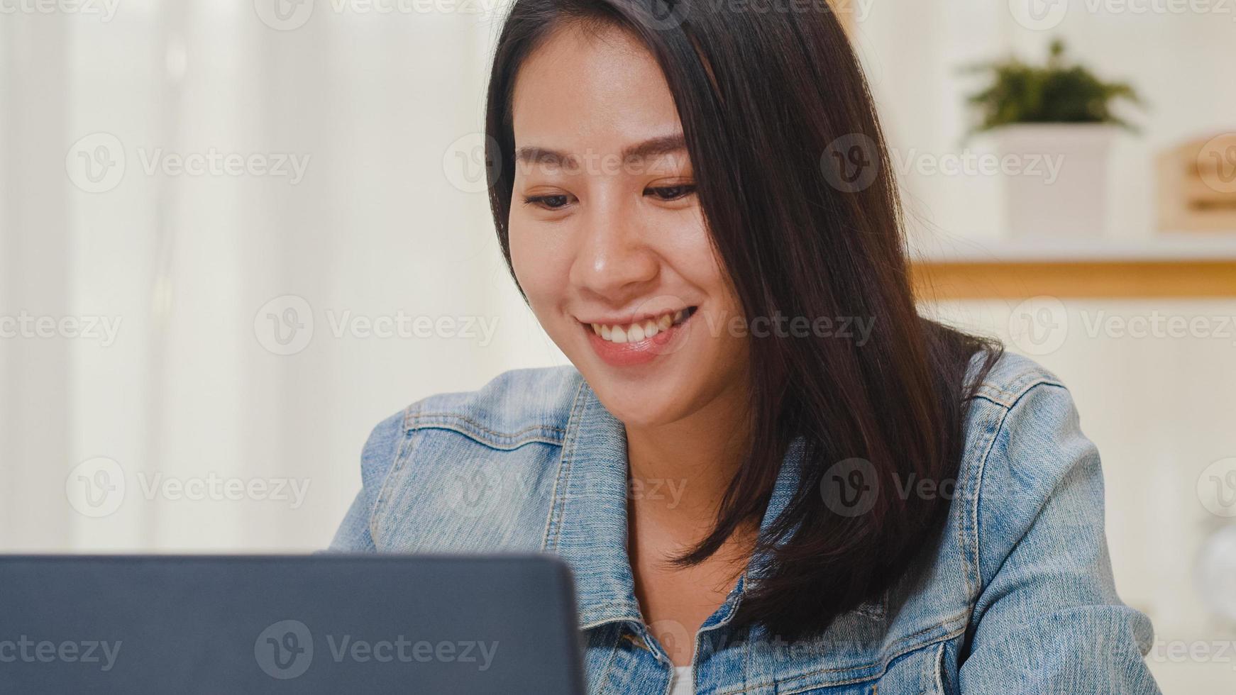 Retrato de ropa casual de mujeres de negocios inteligentes independientes usando laptop trabajando en el lugar de trabajo en la sala de estar en casa. feliz joven asiática relajarse sentado en la búsqueda de escritorio y hacer trabajo en internet. foto