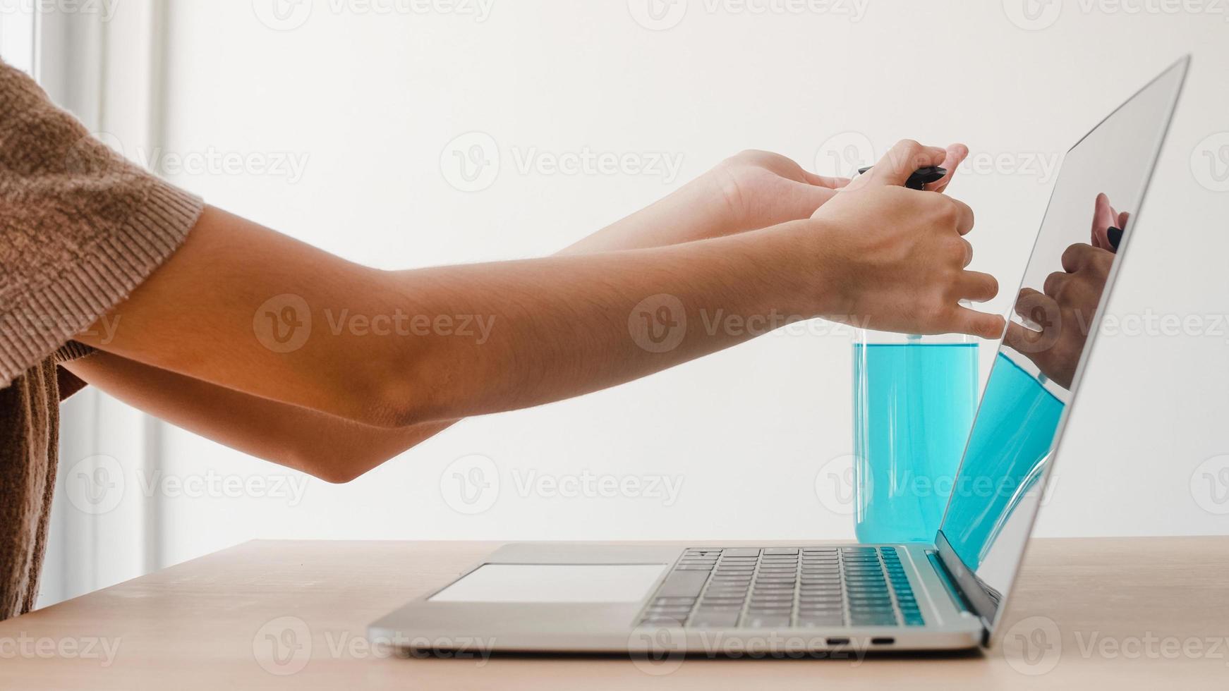 Mujer asiática que usa alcohol gel desinfectante lavarse las manos antes de trabajar en la computadora portátil para proteger el coronavirus. Las mujeres empujan el alcohol para limpiar por higiene cuando el distanciamiento social se queda en casa y el tiempo de auto cuarentena. foto