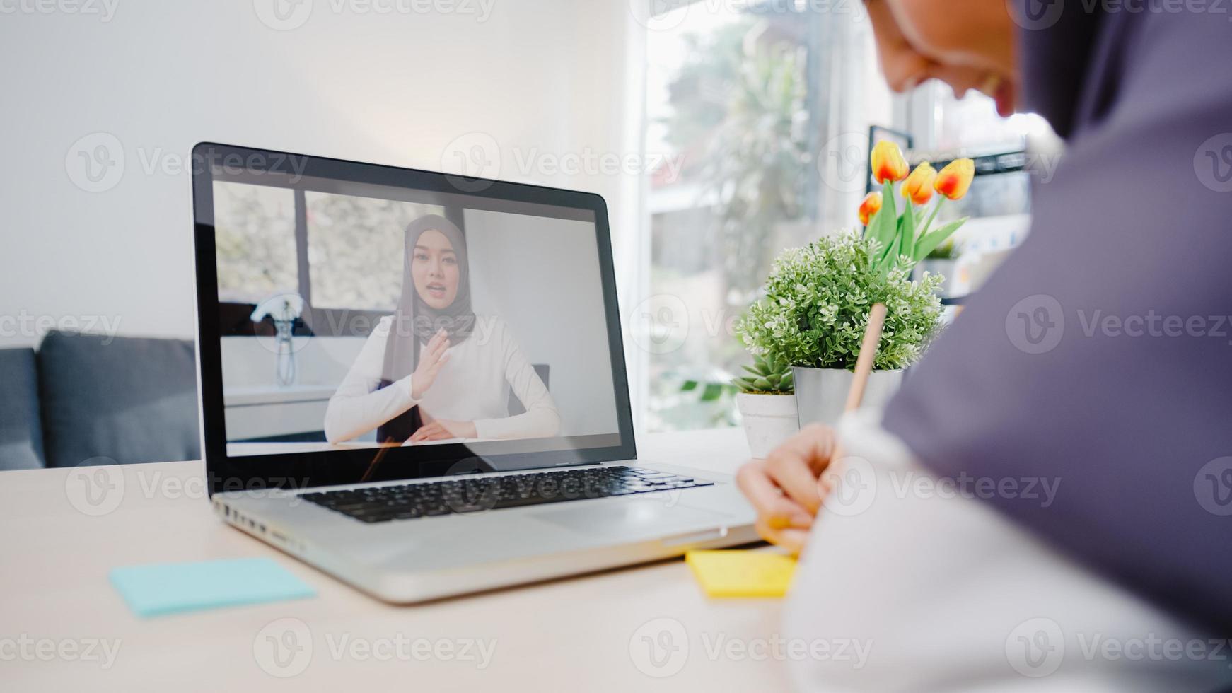 Asia muslim businesswoman using laptop talk to colleague about plan by video call brainstorm online meeting while remotely work from home at living room. Social distancing, quarantine for corona virus photo