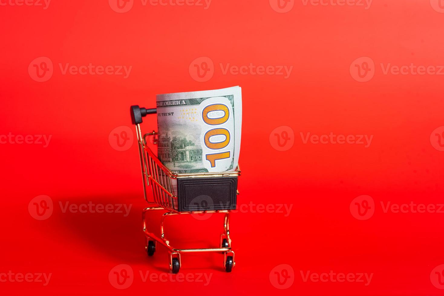 dólares de dinero en un carrito de compras sobre un fondo rojo. Descuentos y Black Friday. foto
