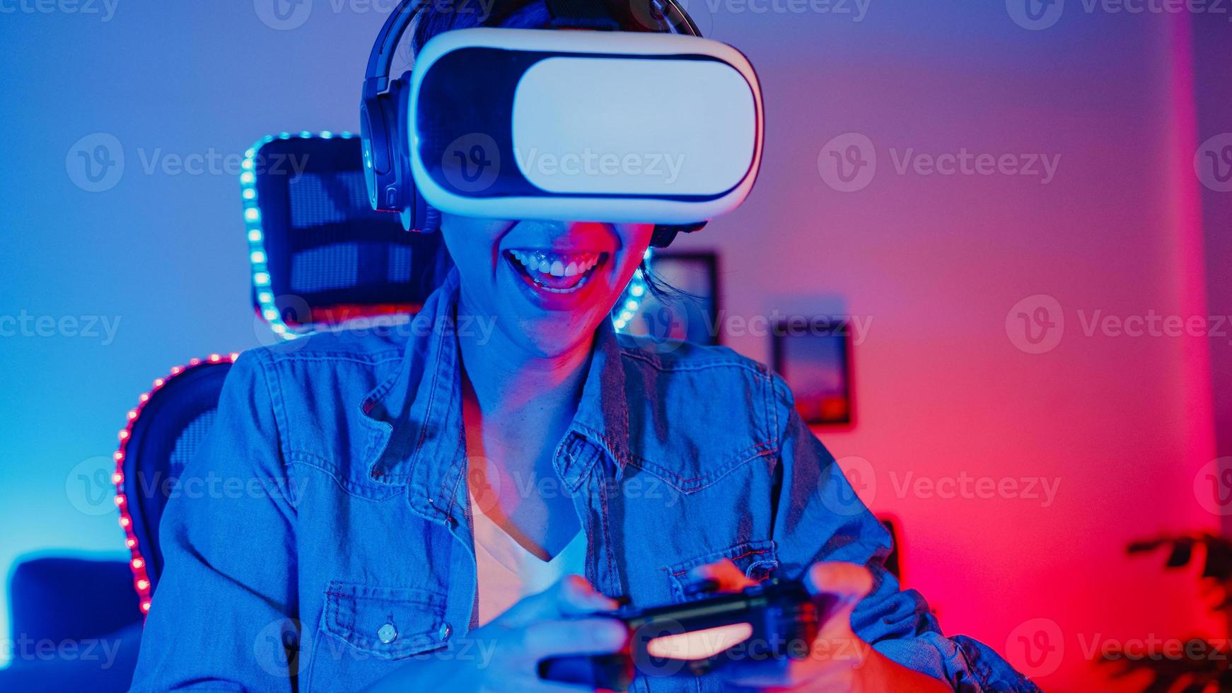 feliz joven asia chica gamer ganadora usa gafas de realidad virtual, auriculares y controlador de joystick divertido y emocionado con el juego en línea en el estudio de neón en casa por la noche, actividad de cuarentena en casa. foto