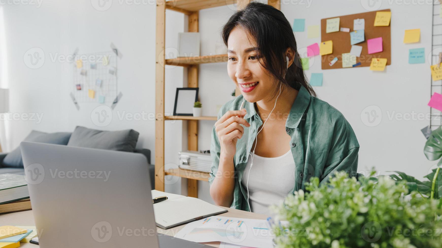 Asia businesswoman using laptop talk to colleagues about plan in video call while smart working from home at living room. Self-isolation, social distancing, quarantine for corona virus prevention. photo