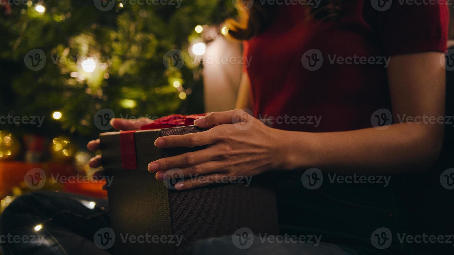 Young Asia female having fun opening X'Mas present box near Christmas tree decorated with ornaments in living room at home. Merry Christmas night and Happy New Year holiday festival. photo