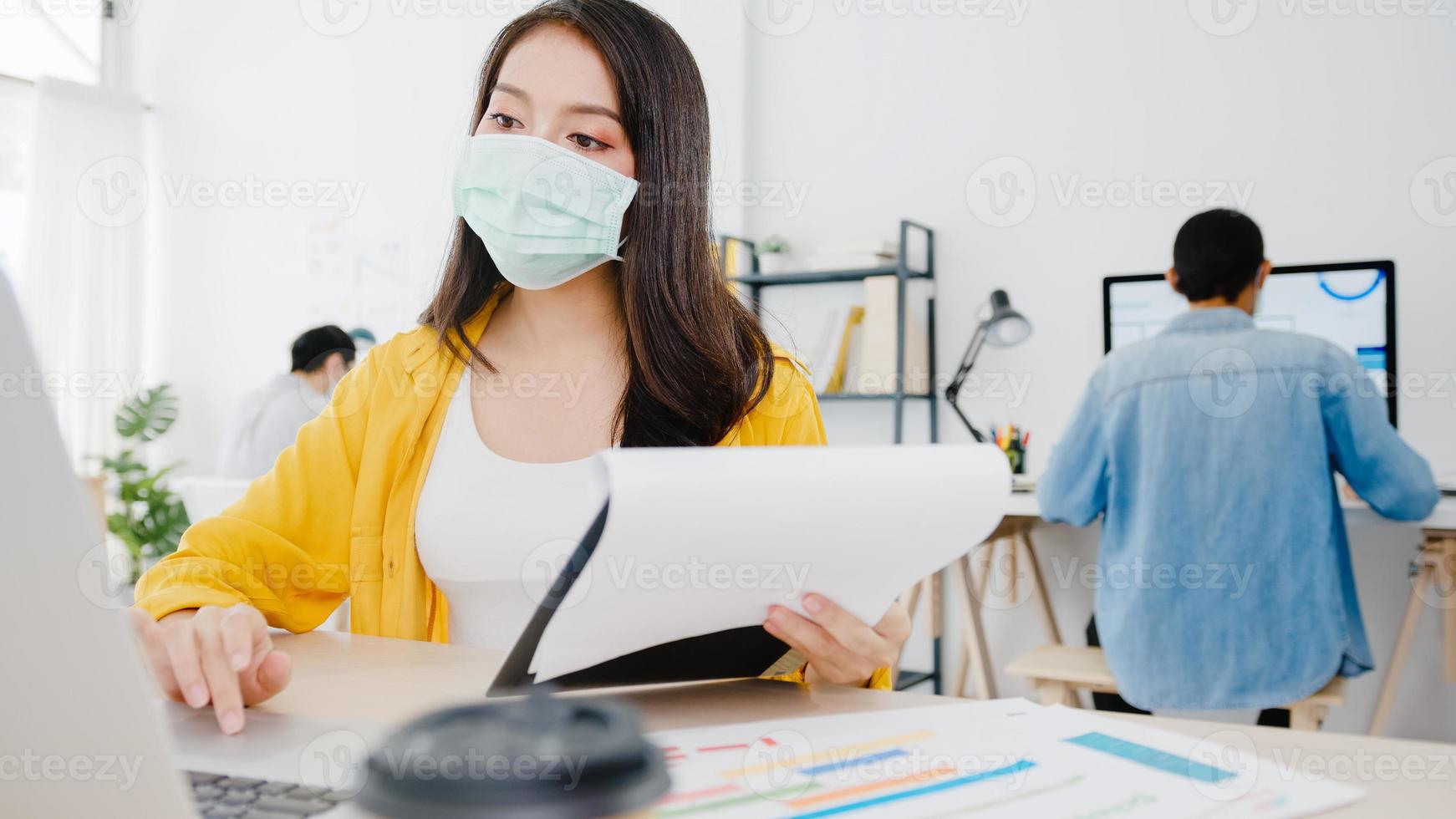 Asia empresaria emprendedora con mascarilla médica para el distanciamiento social en una nueva situación normal para la prevención de virus mientras usa la computadora portátil en el trabajo en la oficina. estilo de vida después del virus corona. foto