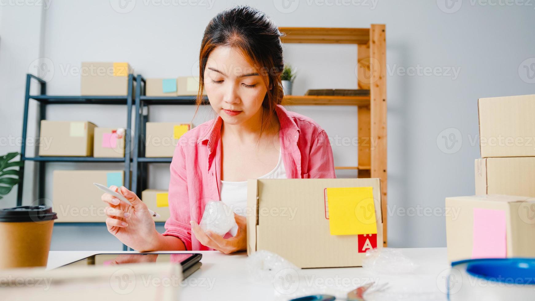 Young Asia entrepreneur businesswoman check product purchase order on stock and save to tablet computer work at home office. Small business owner, online market delivery, lifestyle freelance concept. photo