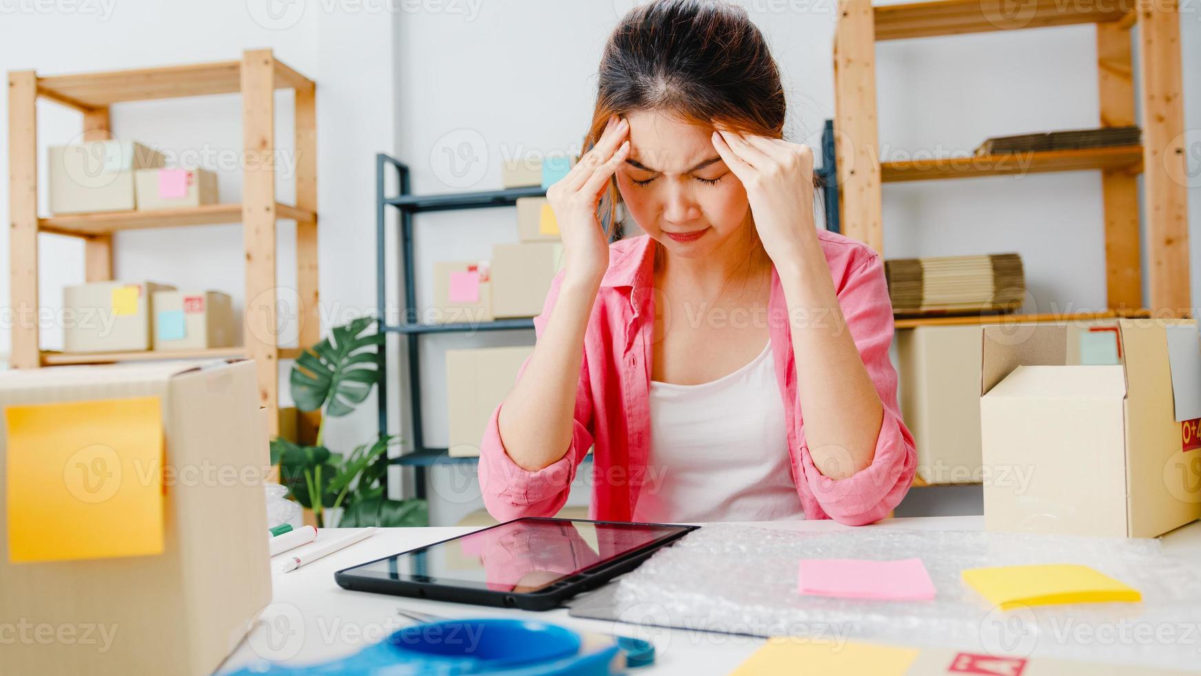 joven empresaria empresaria de asia comprobar la orden de compra del producto en stock, utilizando la sobrecarga de trabajo duro de la tableta en la oficina en casa. propietario de una pequeña empresa, entrega de mercado en línea, concepto independiente de estilo de vida. foto