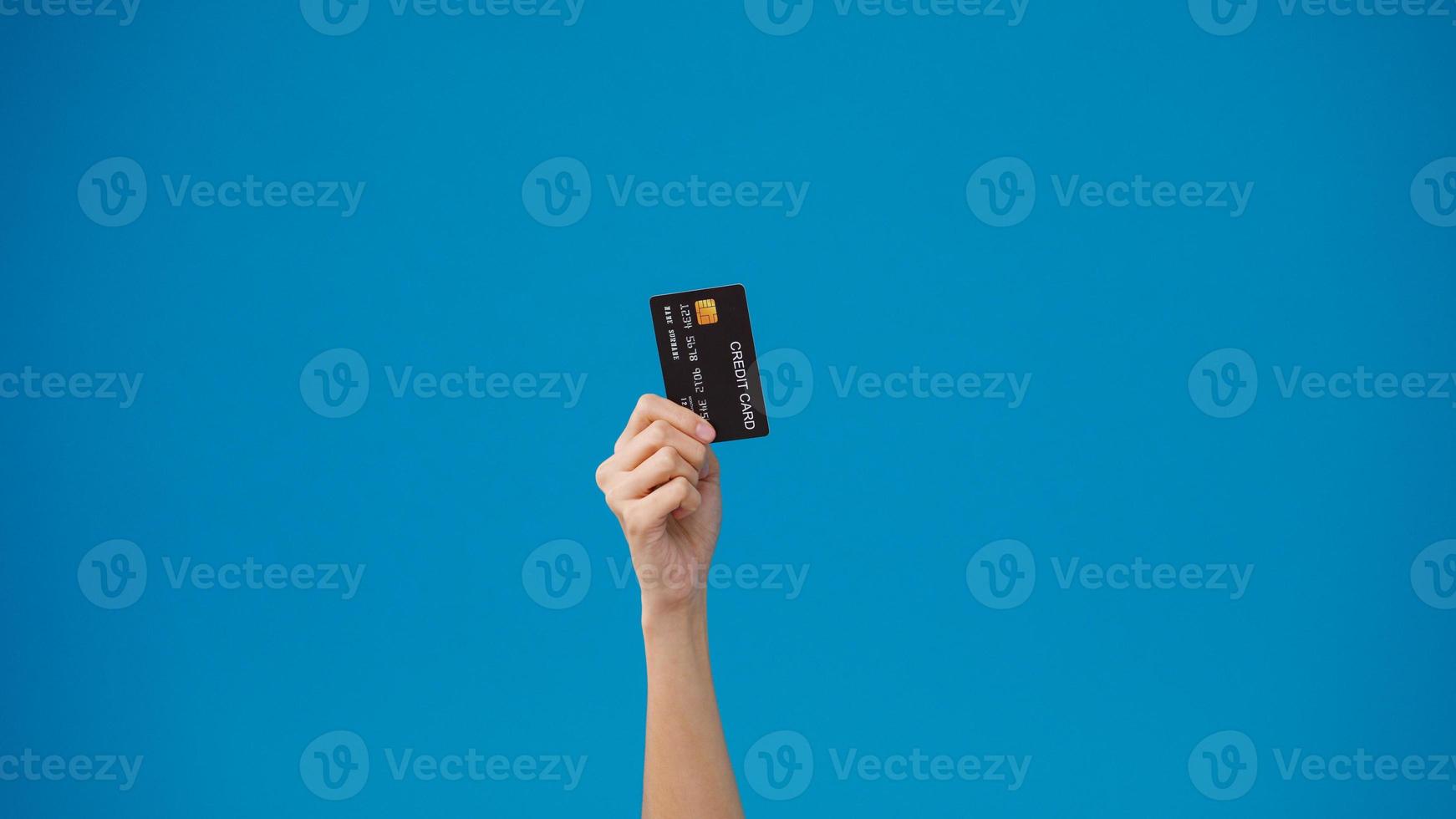 Young woman hand shows credit card for shopping online over blue background in studio. Copy space for place a text, message for advertisement. Advertising area, mockup promotional content. photo