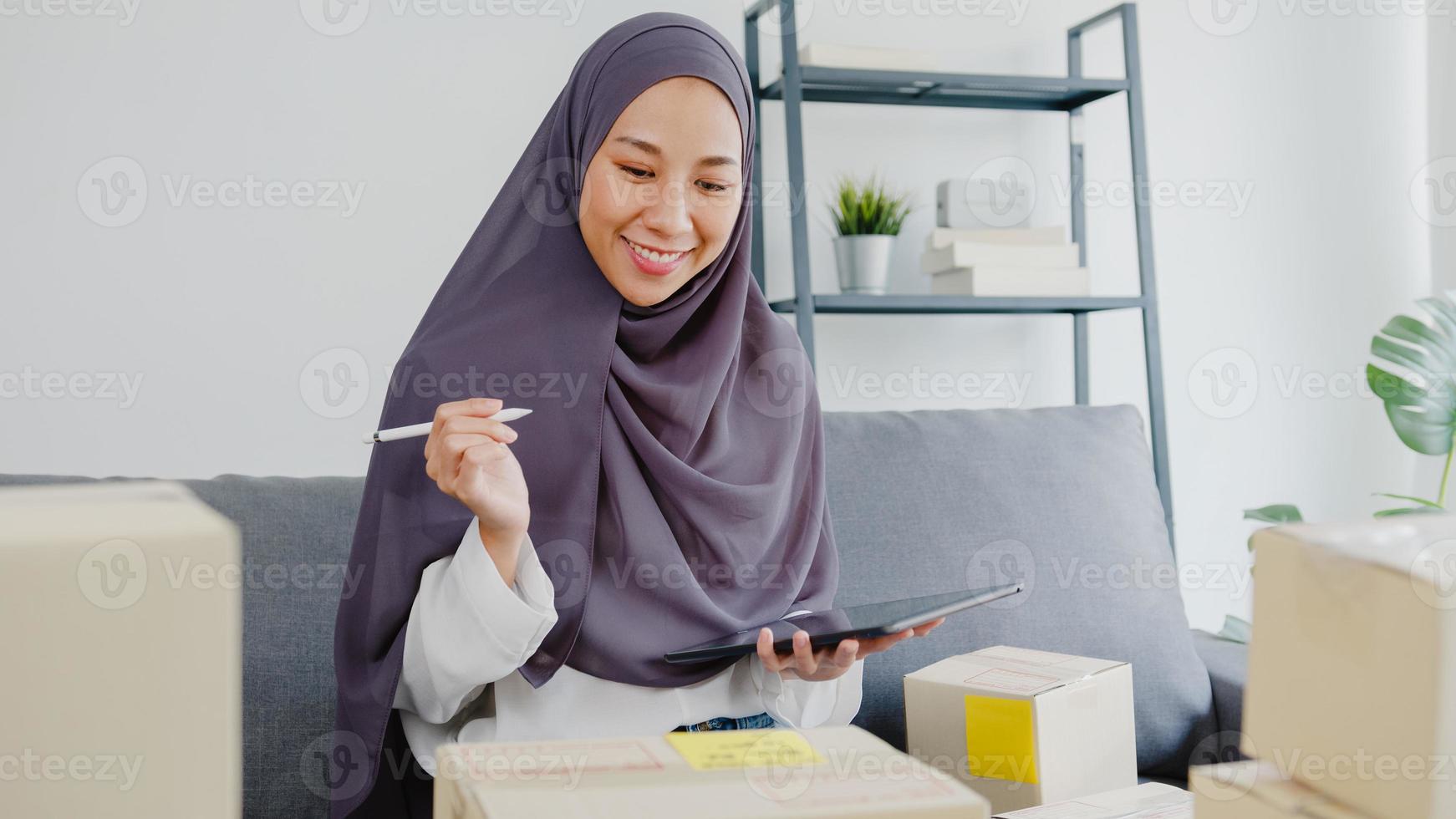 Young Asia muslim businesswoman check product purchase order on stock and save to tablet computer work at home office. Small business owner, online market delivery, lifestyle freelance concept. photo