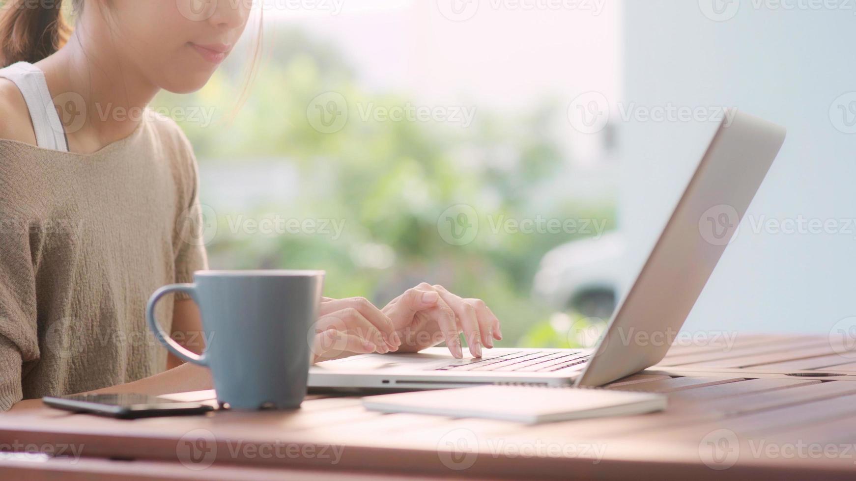 Freelance Asian woman working at home, business female working on laptop sitting on table in the garden in morning. Lifestyle women working at home concept. photo