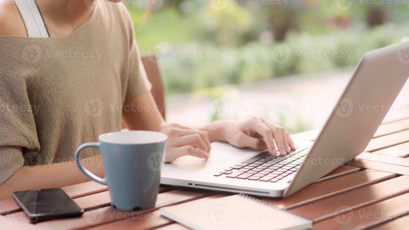 Freelance Asian woman working at home, business female working on laptop sitting on table in the garden in morning. Lifestyle women working at home concept. photo