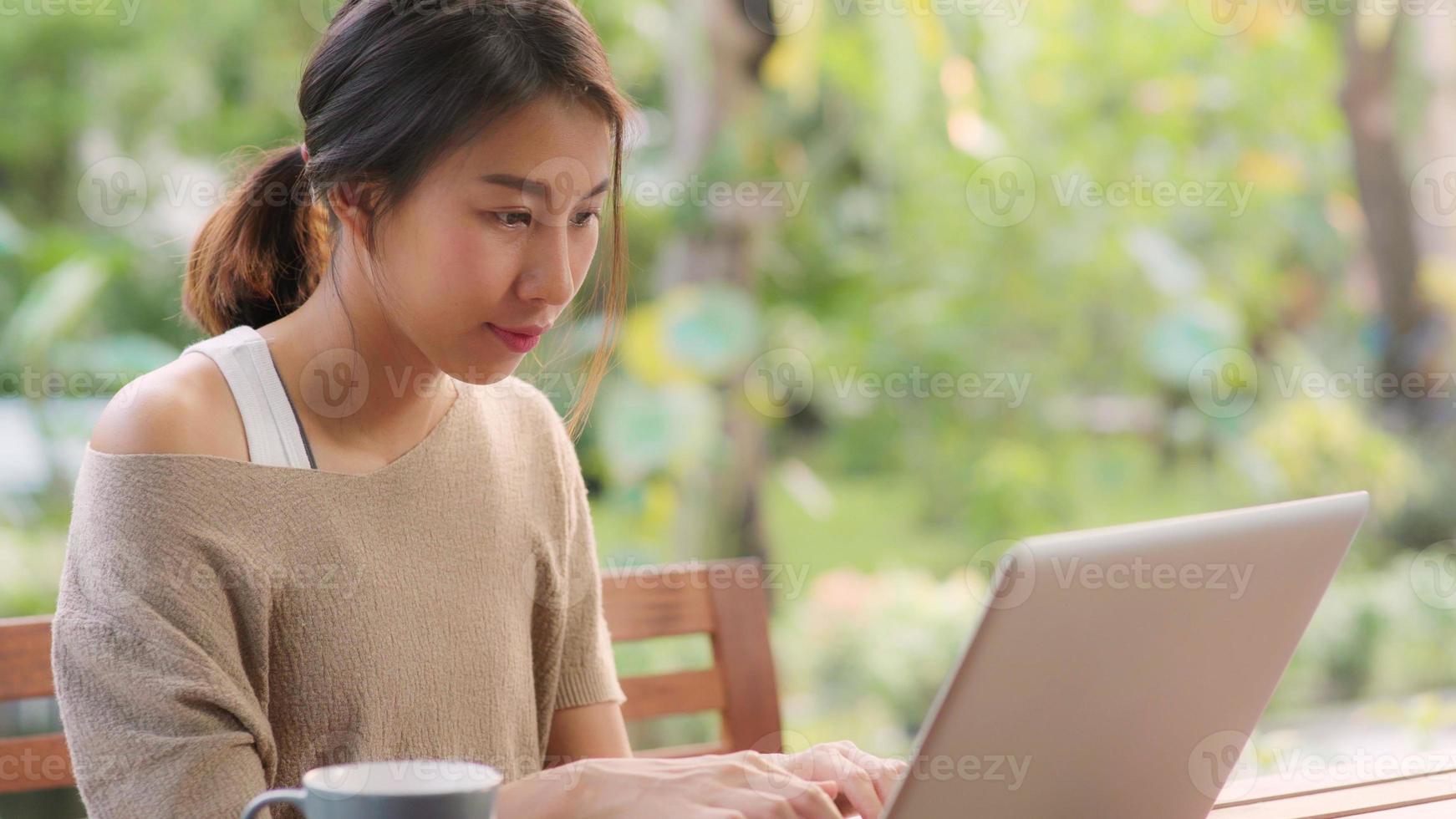 mujer asiática independiente que trabaja en casa, mujer de negocios que trabaja en la computadora portátil sentada en la mesa en el jardín por la mañana. mujeres de estilo de vida que trabajan en el concepto de hogar. foto