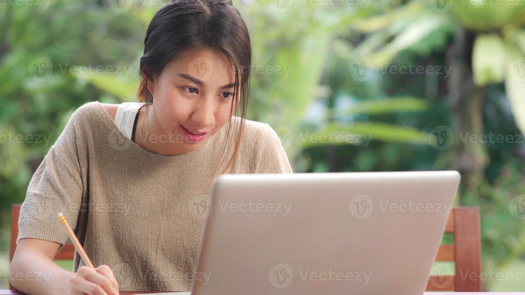 mujer asiática independiente que trabaja en casa, mujer de negocios que trabaja en la computadora portátil sentada en la mesa en el jardín por la mañana. mujeres de estilo de vida que trabajan en el concepto de hogar. foto