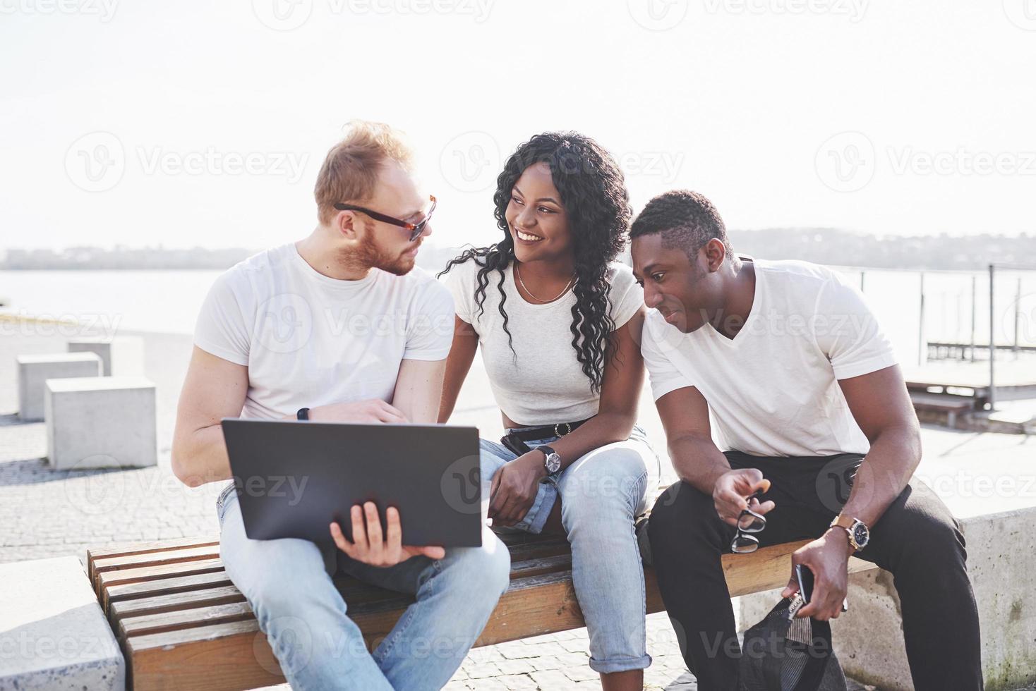 hermosos amigos multiétnicos usando una computadora portátil en la calle. concepto de estilo de vida juvenil foto