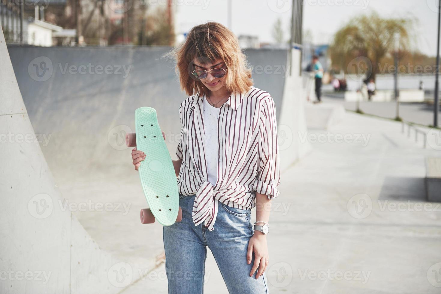 elegante y bella mujer joven con una patineta, en un hermoso día soleado de verano. foto